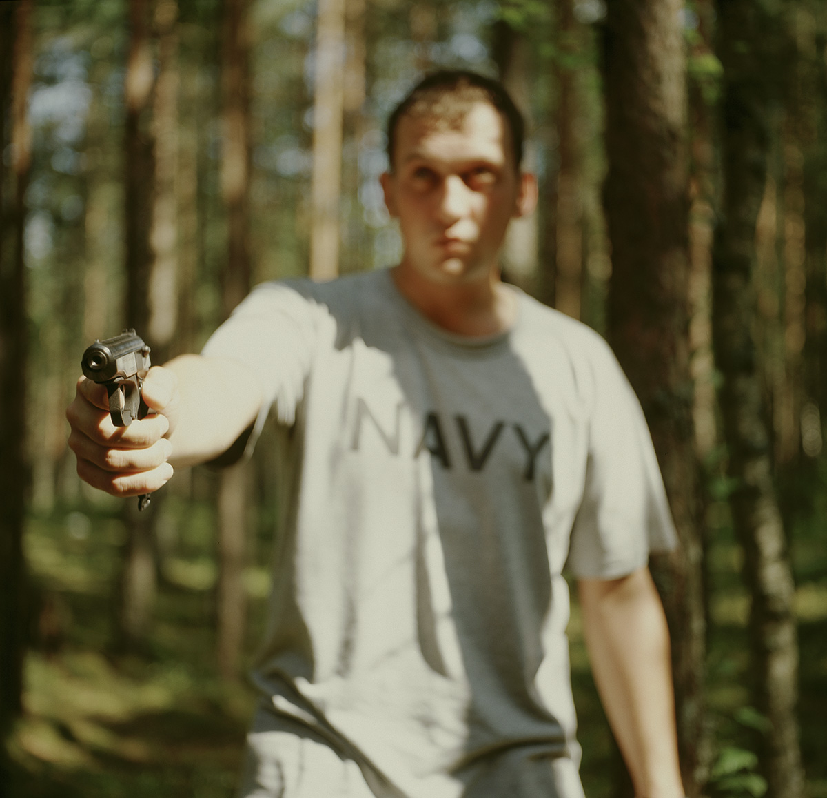 Boy in navy t-shirt in the forest pointing gun